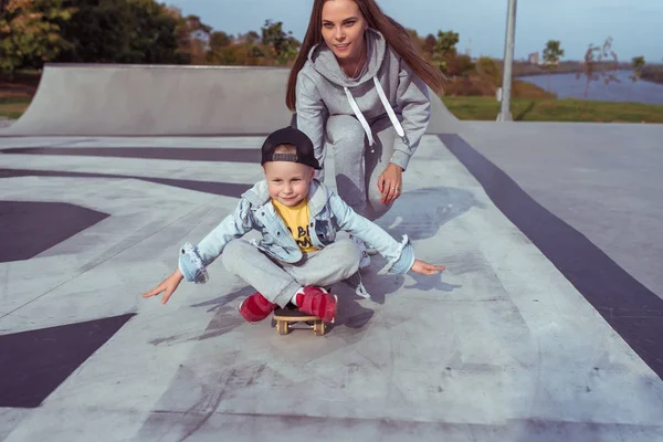 Ibu muda mengajar skateboard, anak kecil, skateboard. Istirahat pada akhir pekan di jalan di taman. Setiap hari hangat pakaian, musim gugur hari — Stok Foto