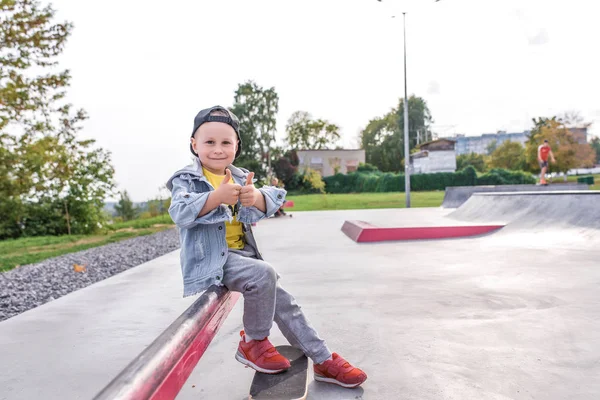 Anak laki-laki berusia 3-5 tahun, belajar untuk naik skateboard, hari musim gugur, pakaian hangat biasa. Denim dengan topi baseball. Belajar mengemudi, pengalaman pertama, olahraga di luar ruangan. Ruang kosong untuk menyalin teks . — Stok Foto