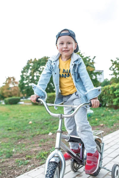 Liten pojke 3-5 år gammal, lär sig cykla, höst dag, casual varma kläder. Denim med basebollkeps. Körlektioner, första upplevelsen, utomhussport. — Stockfoto
