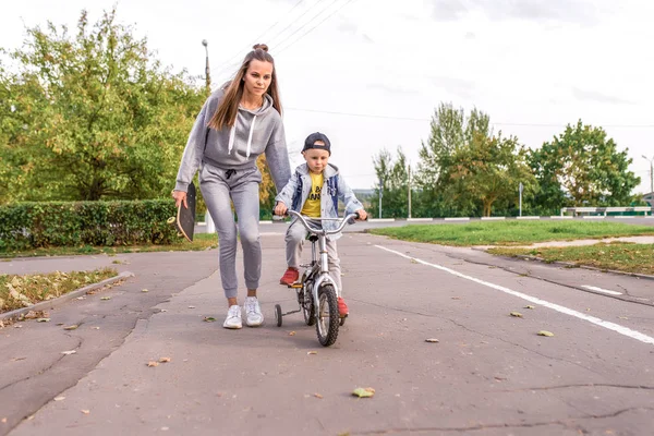 Tânără femeie mama învață copil plimbare cu bicicleta, băiețel fiu. Odihneşte-te în weekend în parc. Hainele calde de zi cu zi, ziua de toamnă. Sprijinirea îngrijirii și educației parentale . — Fotografie, imagine de stoc