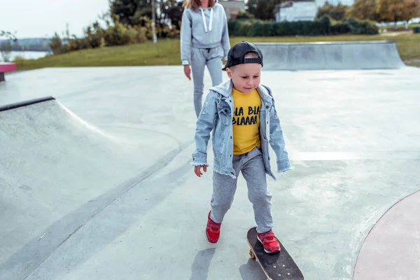 Veselý šťastný chlapeček 3-5 let, v létě na sportovním hřišti, učí se jezdit na skateboardu, emoce radosti, zábavy, odpočinku a radosti. Nenucené oblečení, džínové kalhoty, baseballová čepice. — Stock fotografie
