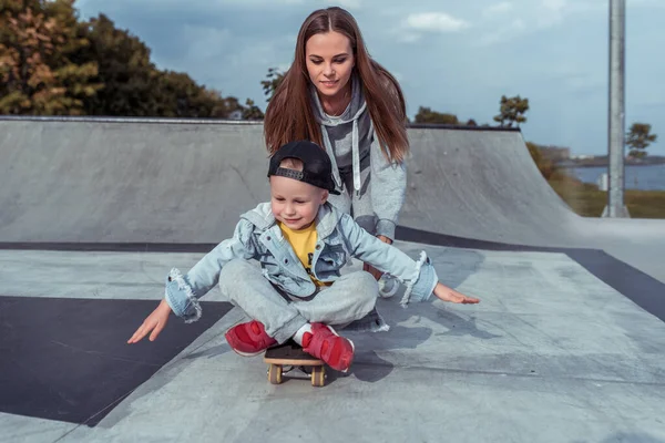 Ibu ibu mengajarkan keseimbangan anak-anak di skateboard, anak laki-laki berusia 3-5 tahun, di kota olahraga musim panas, musim gugur, belajar mengendarai skateboard, emosi sukacita, menyenangkan, santai dan menikmati . — Stok Foto