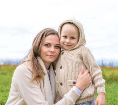 Küçük oğlan çocuğu annesine sarılıyor mutlu gülümsüyor, şefkatli çocuk, sonbahar günü sıcak giysi başlığı, kadın anne çocuğu oynuyor, yaz doğası. Mutlu ol, eğlen, rahatla, neşelen, sev, sev.