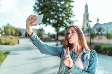 Kotlu bir kız, yazın şehir parkında elinde akıllı telefonuyla fotoğraf çekiyor, selfie çekiyor, internetten video görüşmesi yapıyor. Modern moda ve güzel bir kadın..