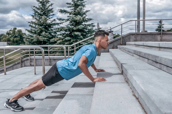 Young sports male athlete, pushing up steps in the summer in the city, workout fitness training, active lifestyle of modern youth, sportswear t-shirt shorts sneakers. Motivation for life. — ストック写真