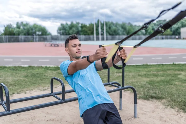 Young sportsman, male athlete, pulls himself on hinges, straps for chest muscles, in summer day in the city, workout fitness, active lifestyle of modern youth, sportswear. Motivation for life. — ストック写真