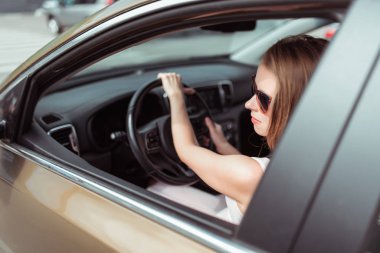 Kadın yazın arabada, aynaya bakıyor, ters dönüyor, kavşağa dönüyor, yaz tatilinde arazi aracı, güneş gözlükleri, trafik sıkışıklığı, trafik çemberi, yaya geçidini atlıyor. Trafik lambasının önünde duruyor.