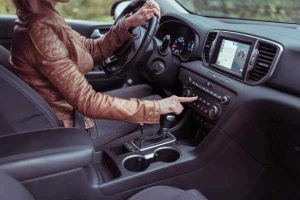 Nő autó belső tartalmaz gomb, alkalmazás légkondicionáló kiválasztás, ülés fűtés szellőztetés, automata sebességváltó, őszi tavaszi erdő park. Bőrdzseki. Navigációs képernyő. — Stock Fotó