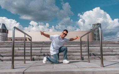 Happy man dancer dancing breakdance, summer in city, cloud background, hip-hop dancer. Youth lifestyle, active, trend modern, fitness sport, positive motivation.