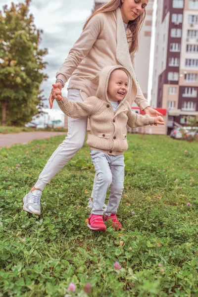 Woman mom holds the child hands, little boy son, autumn in city, warm casual clothes, grass and lawns building background. Happy smiling have a rest weekend. — Stok fotoğraf