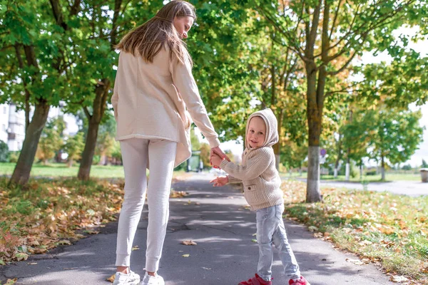 Mladá rodina, žena matka drží svého syna za ruku, malý chlapec se otočí a ohlédne se. Emoce radosti, úsměvu a relaxačního víkendu, procházka podzimním parkem ve městě. Teplé příležitostné oblečení. — Stock fotografie