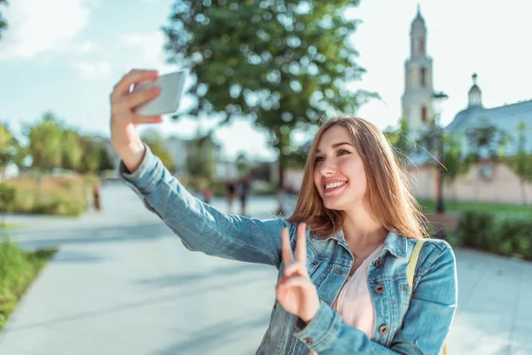 Happy girl s'imagine au téléphone, selfie sur smartphone, veste en denim, été dans le parc de la ville. Des émotions de bonheur, des joies de détente amusante. Enregistrer des messages vidéo, appel en ligne dans l'application Internet . — Photo