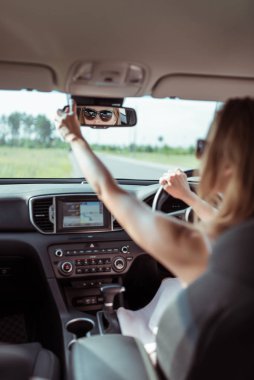 Araba süren, dikiz aynasından bakan, geri geri giden, alışveriş merkezine park eden, garaja araba süren bir kadın. Otomatik vites. Araç içi. Elbiseli yaz kızı..