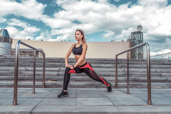 Athletic girl gjør det å strekke seg før jogging, sommer i byen, livsstil motivasjon, trening og trening på gaten. Skyete trappebakgrunn. Sportstøy på toppen . – stockfoto