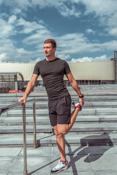 Male athlete, in the summer in the city, training muscles and warming up before jogging, in the morning in the city. Sportswear. Motivation and lifestyle of youth. Cloud stair background. — ストック写真