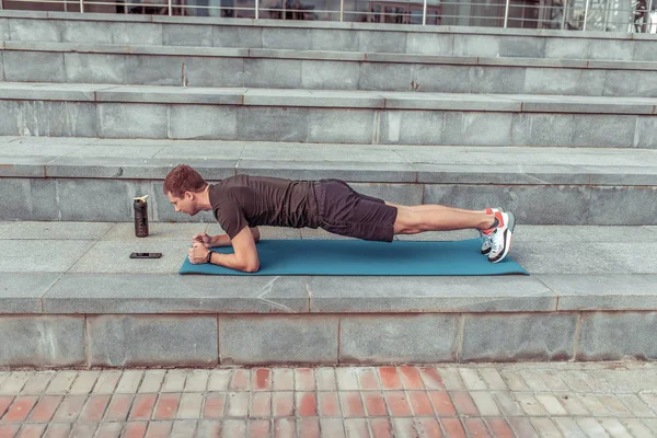 Male athlete summer city training abdominal muscles press stands on Plank yoga ma, morning in city. Sportswear Motivation lifestyle youth. Steps background smartphone timer shaker with protein water. — ストック写真