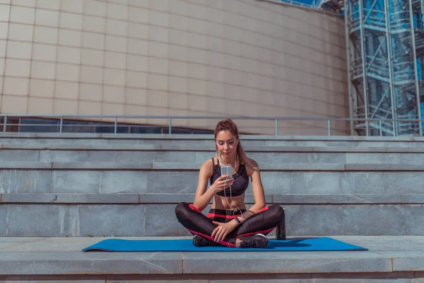 Дивовижна сучасна спортивна дівчина слухає навушники смартфонів Yoga Mat. Відпочивайте після літнього тренування міського життя мотивації. Текст копіювання вільного простору, Reads and write sms. — стокове фото
