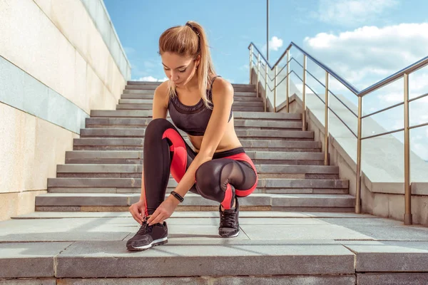 Mulher atlética bonita amarrando atacadores em tênis, correndo de manhã, fundo escadas na cidade no verão, estilo de vida motivação. Sportswear leggings top, figura bronzeada . — Fotografia de Stock