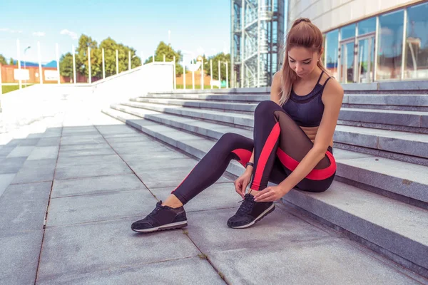 Beautiful athletic woman resting after workout tying shoelaces sneakers, jogging morning, stairs background summer motivation lifestyle. Sportswear leggings top, tanned figure. Free space copy text.