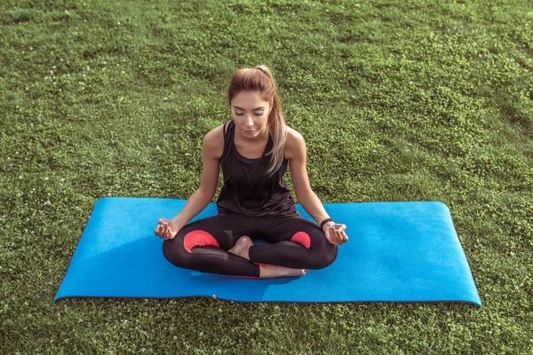 Красива дівчина тренується в місті, роздумуючи, сидячи на килимку йоги. Фітнес тренування активний спосіб життя. Жінка атлетичної фігури. Прибуття в тишу спокійна гармонія розуму і тіла в медитації . — стокове фото