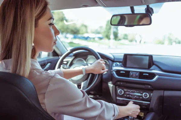 Woman driving a car, in summer in parking lot near a shopping center. Reversing, interior of car, looking in the side view mirror. Automatic transmission. Parking in the garage. — Stock Photo, Image