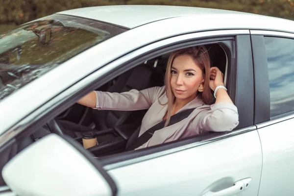 Beautiful girl in a car interior driving. In summer in city. Happy smiles. Car sharing car for rent. Business sedan in white. Parking in parking lot. Emotions of comfort pleasure, close-up.