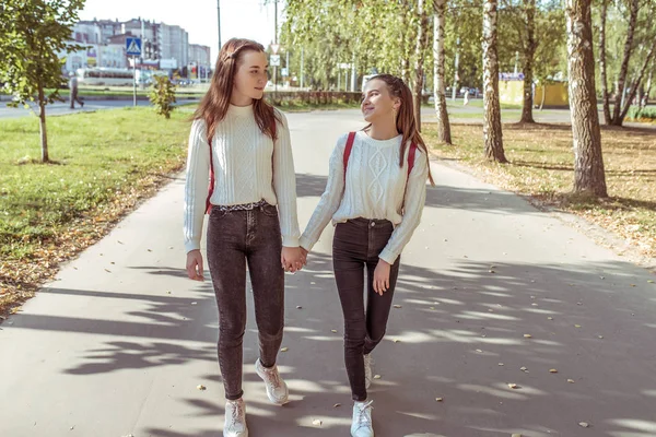 2 girls, schoolgirls, teenagers 13-15 years old, autumn day, summer in city, walking by hand, happy smiling. Fun and pleasure best girlfriends. They return after school on street. Casual wear. — 스톡 사진
