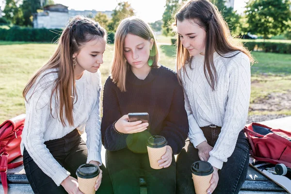 Три девочки школьницы подростки 12-14 лет, осень день летний город смотреть видео смартфон, онлайн-приложение социальных сетей Интернет. Лучшие подруги расслабляются после школы в теплых вязаных свитерах . — стоковое фото