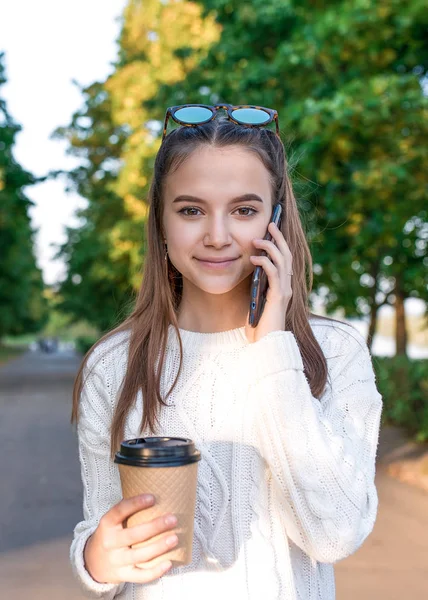 12-15岁的少女，秋天的一天，街上的肖像，电话，公园里的夏天。 听下面的留言。 一杯咖啡茶，笑容满面。 打电话给父母。 养育子女的概念. — 图库照片