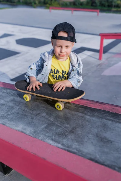 Anak laki-laki berusia 3-5 tahun, anak-anak skate, skateboard, istirahat akhir pekan, pelatihan pendidikan, langkah-langkah pertama di papan tulis. Di musim panas di kota. Pakaian santai, jeans. Happy tersenyum sukacita dan bersenang-senang . — Stok Foto