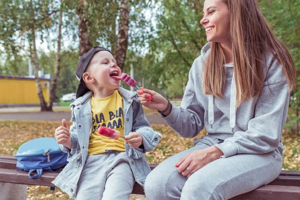 Glad glad ung familj, liten pojke 3-5 år gammal, mor kvinna, Ät rosa glass på en pinne. Sommar i stan, höstdag. Fritidskläder, jeans. Känslor av glädje helg kul och avkoppling. — Stockfoto