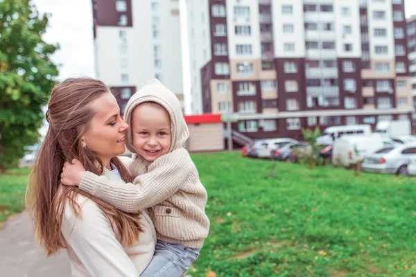 Kadın anne, çocuğuyla yürüyor, 4-5 yaşlarında, güz günü sokağı, mutlu insanlar oynuyor, eğleniyor ve gülüyor, kapüşonlu, mutlu, sıcak günlük giysiler giyiyor. Metni kopyalamak için boş alan.