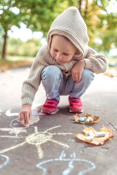 Маленький мальчик 3-5 лет, счастливый рисует красочные карандаши на тротуаре, творчество в парке, чувствовать себя счастливым. Обычная теплая одежда с капюшоном. Осенний день. Эмоции счастье и удовольствие . — стоковое фото