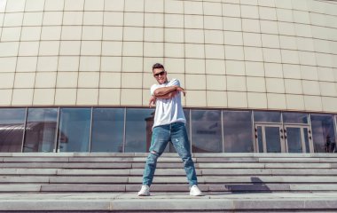 Mutlu adam gülümsüyor, genç adam dansçı, yazın şehirde, dans eden sokak dansı, modern gençlik tarzı. Moda ve fitness sporu. Metni kopyalamak için boş alan. Adım bulutu arkaplanı.