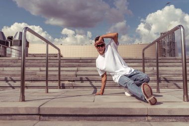Dansçı genç bir adam, yazın şehirde dans ediyor, sokak dansları yapıyor, break dans yapıyor, modern gençlik tarzı. Moda ve fitness sporu. Metni kopyalamak için boş alan.