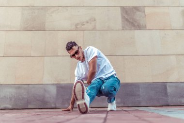 Genç bir erkek dansçı, yazın şehirde, dans eden sokak dansları, modern gençlik tarzı. Moda ve fitness sporu. Tişört gözlükleri ve kot ayakkabıları. Metni kopyalamak için boş alan.