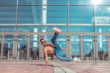 Erkek break dansçı, kaslı gövde, dansçı, genç adam, yaz şehri, dans eden sokak dansları, modern gençlik tarzı. Moda ve spor motivasyonu. Metni kopyalamak için boş alan. Arka plan cam kapıları.