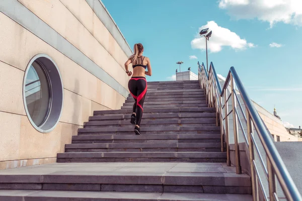 Mulher corre no verão na cidade em escadas, treinamento de fitness e treino. Vista de trás, top leggings sportswear, fundo escada edifício. Espaço livre para motivação de texto de cópia . — Fotografia de Stock