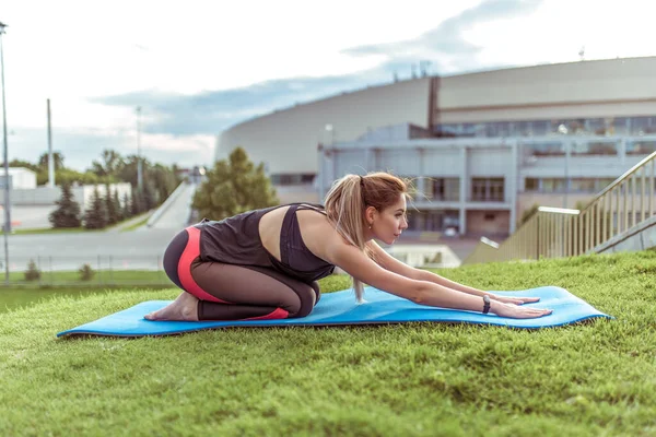 Жінка на йога мат, влітку в місті, тренує і розтягує м'язи. Спортивний одяг, медитація та практика асан. Вільний простір для мотивації копіювання тексту. Фон зелена трава . — стокове фото