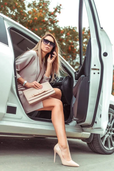 Mujer moderna de moda sale del coche, clase de negocios, zapatos de tacón alto traje formal, taxi en verano de la ciudad, coche compartido, taxi VIP, chica en gafas de sol, estacionamiento. Sonando en el teléfono celular . —  Fotos de Stock