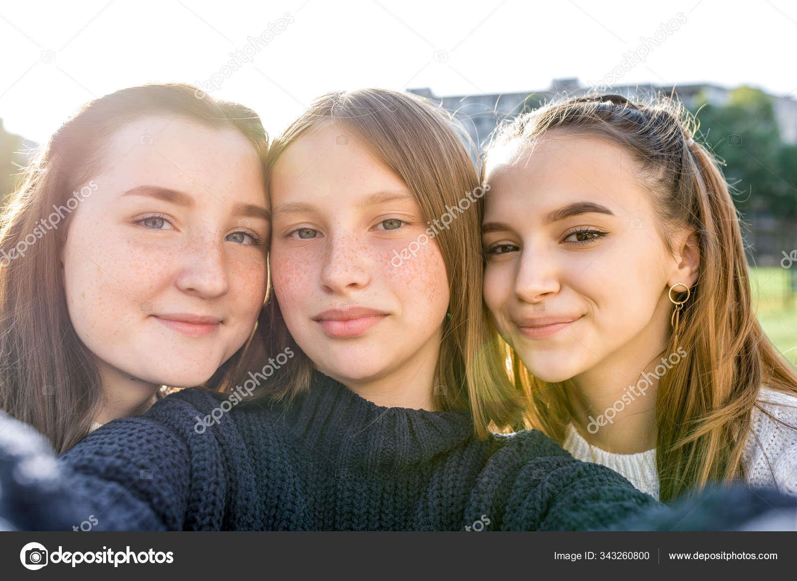 девочки 12-14 лет Три девочки-подростки 12-14 лет, летний город смотрит видео-телефон,  радуются счастливые улыбающиеся люди. Портрет селфи крупным планом. Обычная  одежда, свитера. Эмоции позитивного расслабления . — Стоковое фото © byswat  #343260800