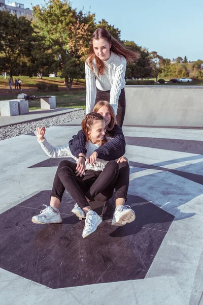Tiga gadis remaja gadis sekolah 12-14 tahun, di musim panas di kota, naik skateboard, bahagia tersenyum, bersenang-senang bersukacita. Liburan akhir pekan. Pakaian santai, sweater hangat. Emosi positif dan menyenangkan — Stok Foto