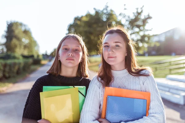 Duas meninas namoradas colegiais 12-14 anos, retrato de verão na cidade na rua, em mãos de cadernos pastas livros didáticos, descansando depois da escola no intervalo da faculdade. Emoções de prazer positivo . — Fotografia de Stock