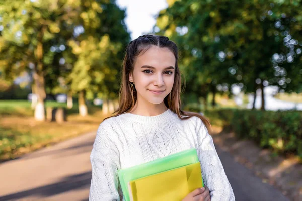 Красивая счастливая школьница, летний портрет в городе на улице в парке, в руках тетради и папки с учебниками, отдыхающие после школы в колледже на каникулах. Эмоции позитива и удовольствия . — стоковое фото
