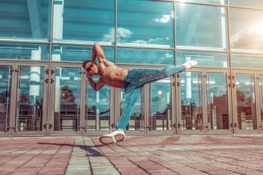 Erkek atlet break dans, atlama, bronzlaşmış spor ve eğitimli gövde. Bir binanın arka plan camları. Şehirde spor motivasyonu.