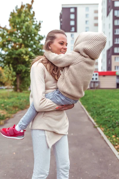 Молода сім'я, жінка, мати тримає сина на руках, ходить з дитиною, хлопчику 4-5 років, осінь у місті, фон будівлі. Емоції щастя, радість від сміху. Повсякденний теплий одяг . — стокове фото