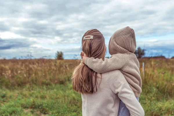 Family woman mother holds her son in her arms, little boy in sweater with hood, rest in field, parenting child care love, parental support. Autumn spring day. Warm clothing. Free space for copy text. — Stock Photo, Image