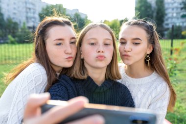 Üç liseli kız öğrenci yaz şehri. Telefondaki fotoğraf, selfie fotoğrafı, online uygulama akıllı telefonu, internetteki sosyal ağlar. Süveter giyme, hava öpücüğü, duygusal rahatlama eğlence eğlencesi..