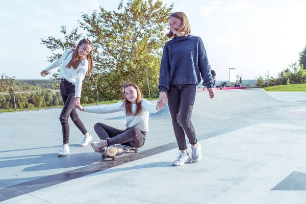 Junge Mädchen im Teenageralter fahren Skateboard im Sommerpark. Lässig trägt er Sweater-Jeans. Emotionen Glück, Spaß, Entspannung, Lächeln Lachen, beste Freundinnen, Erholung nach dem College. — Stockfoto