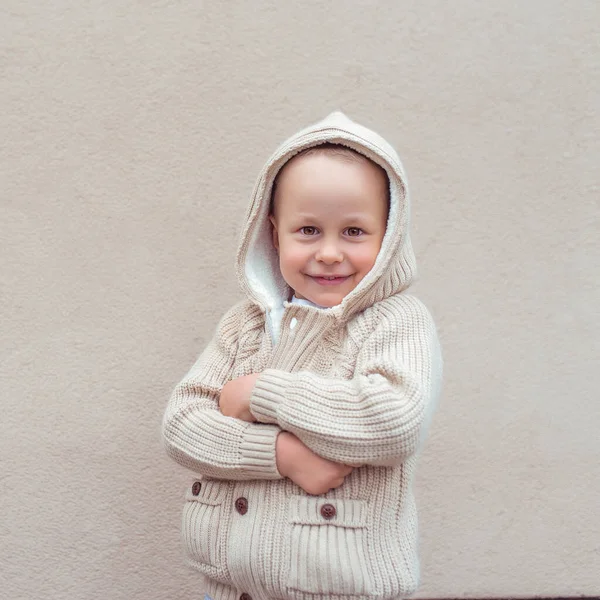 Маленький хлопчик 3-5 років, бежевий фон стіни, емоції радості, веселощів, сміху, сміху, задоволення та щастя. В'язаний теплий светр з капюшоном . — стокове фото